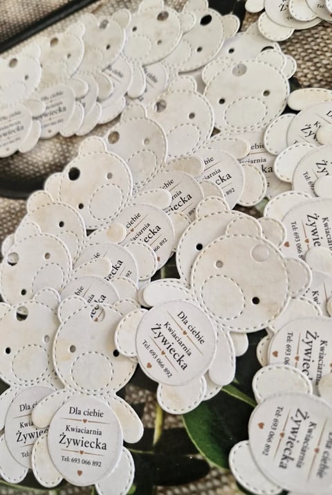 Multiple white circular tags with scalloped edges and printed text, featuring holes for hanging, arranged on a textured surface