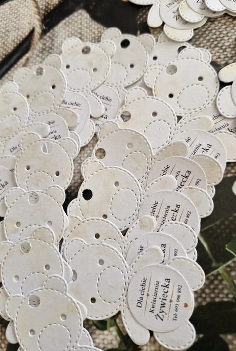 Collection of white scalloped paper tags with holes and printed text, arranged on a neutral fabric surface