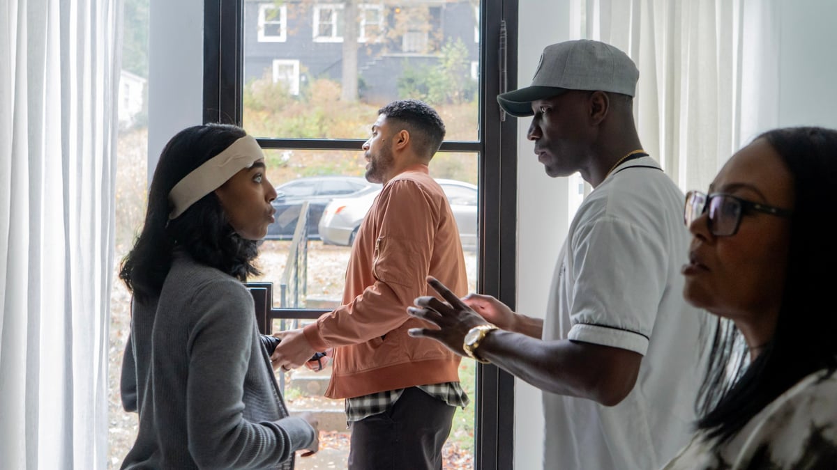 Four people having a conversation indoors near a window with a city street view in the background