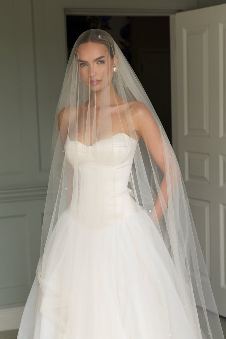 Bride wearing a white strapless sweetheart neckline wedding gown with a long tulle veil adorned with pearls.