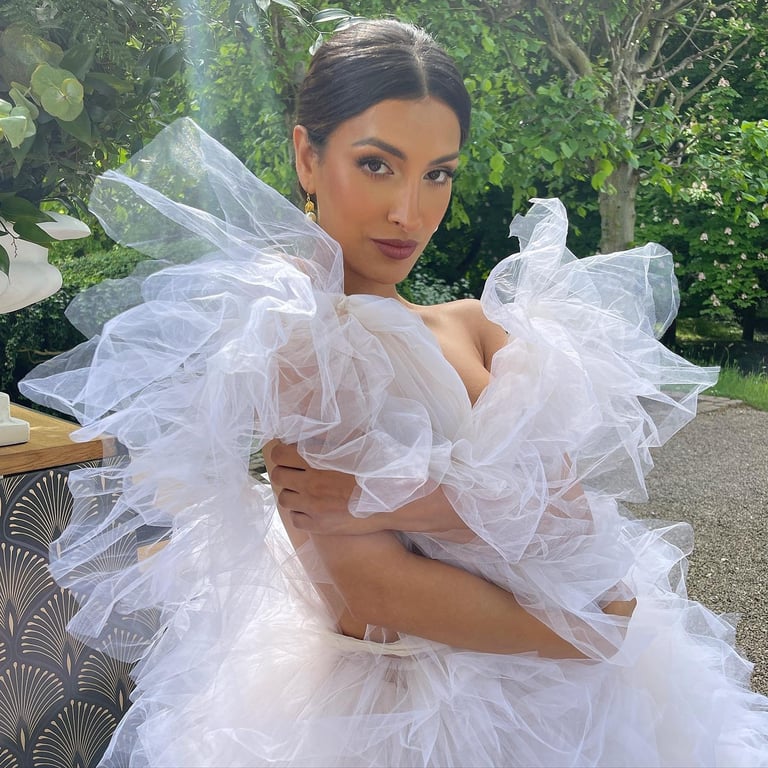 Woman in white tulle ball gown with dramatic ruffled shoulders posing outdoors in garden setting