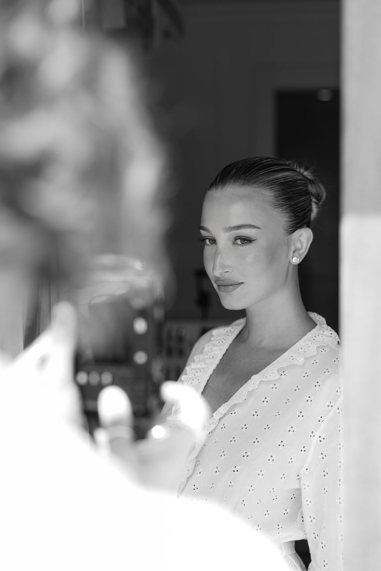 Woman in white textured shirt applies skincare or makeup in bathroom mirror, black and white photograph