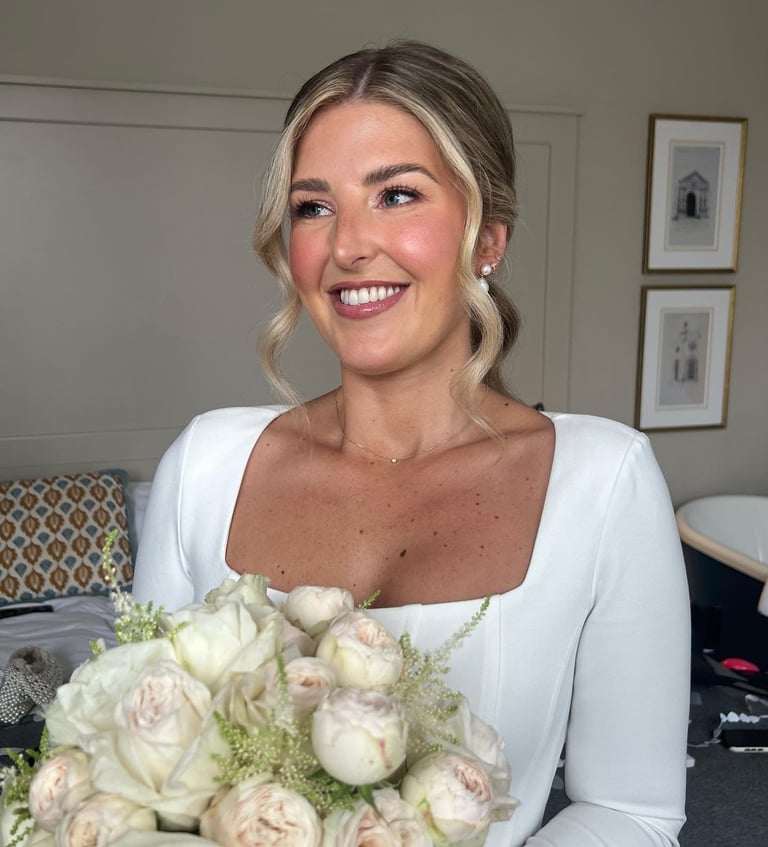 Woman in white dress holding cream and pink rose bouquet, smiling indoors