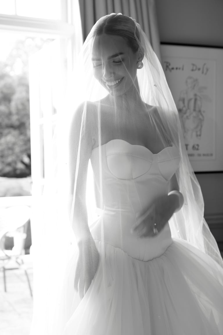 Bride in white sweetheart neckline wedding dress and veil smiling near a window in black and white portrait