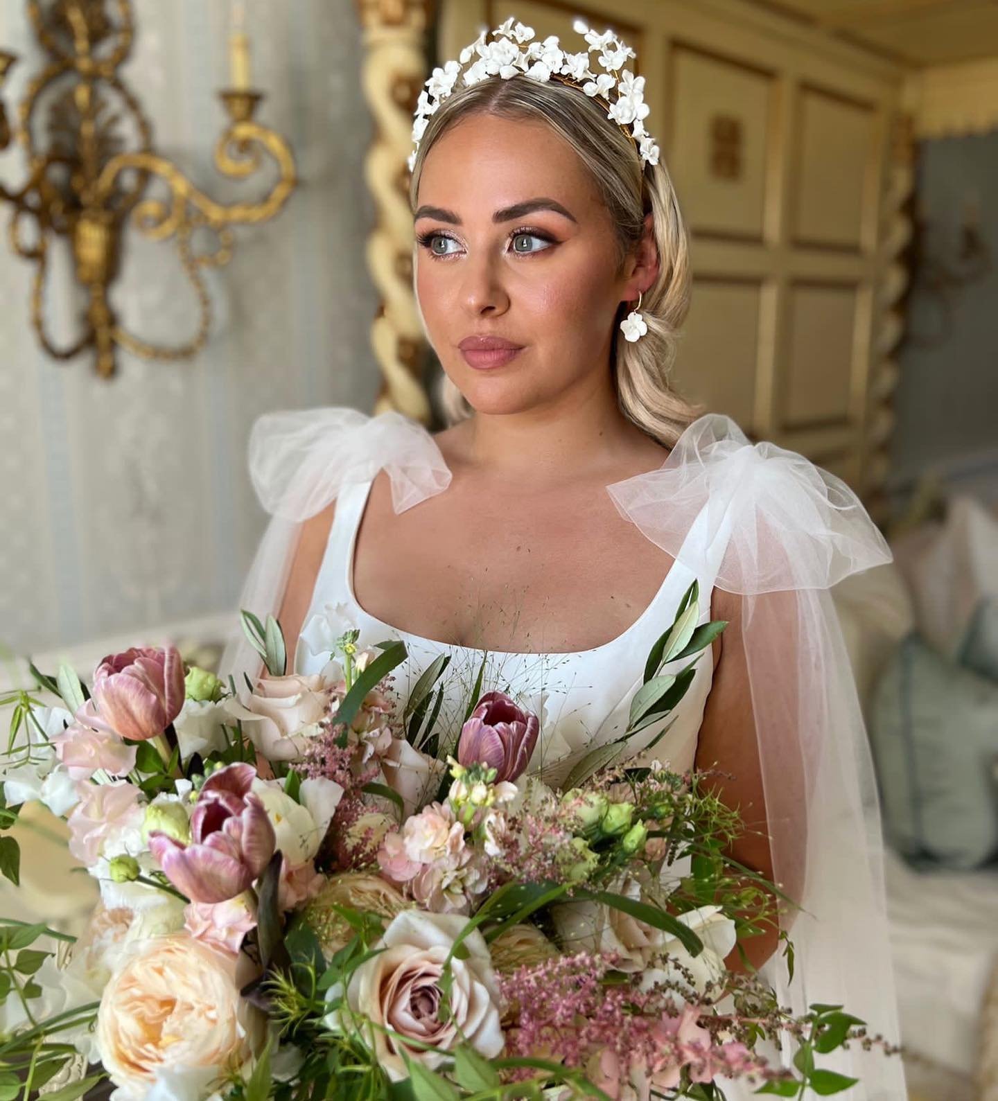 Bride wearing white dress with puff sleeves, tiara, and veil holding pink and cream rose bouquet in elegant interior