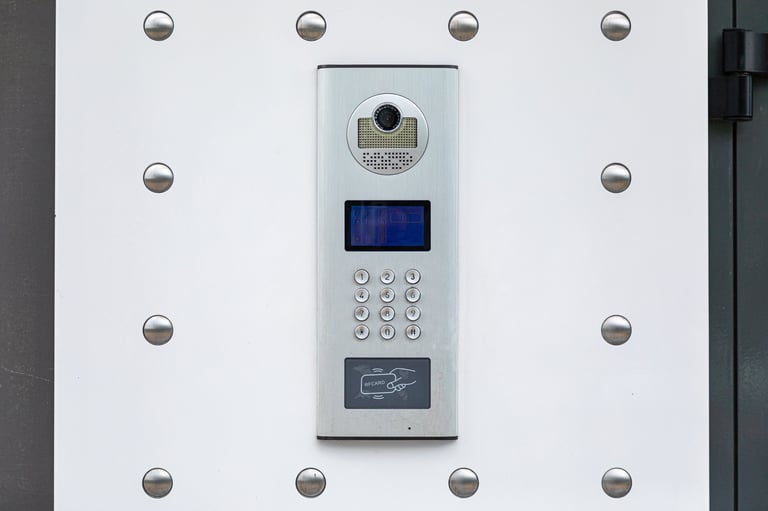 White security intercom panel mounted on wall with camera, blue screen display, numeric keypad, and card reader