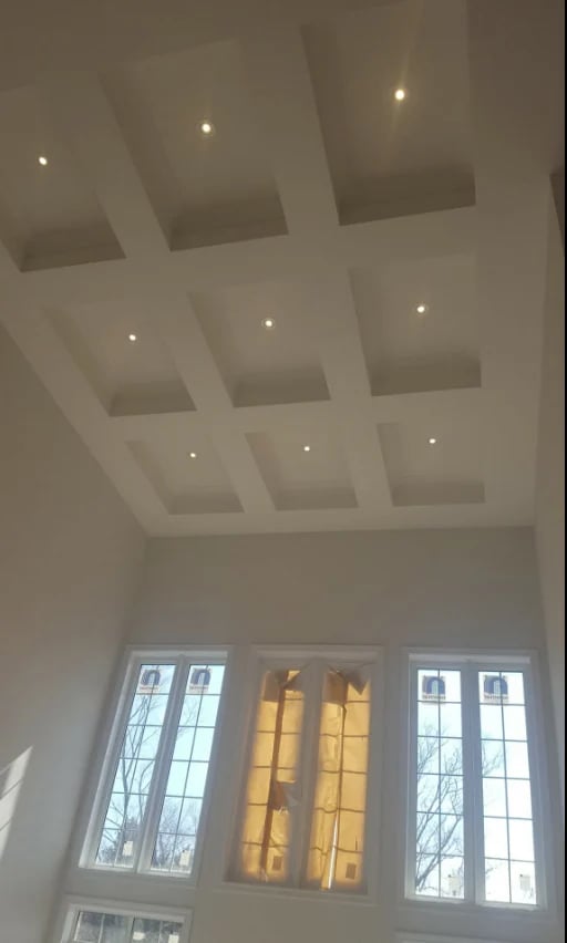 Modern coffered ceiling with recessed lighting and large windows below showing golden sunlight