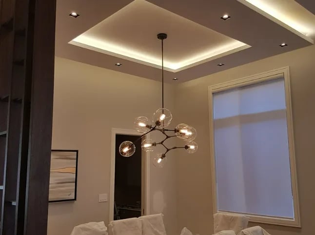 Modern bedroom with geometric pendant light fixture hanging from recessed ceiling with ambient lighting
