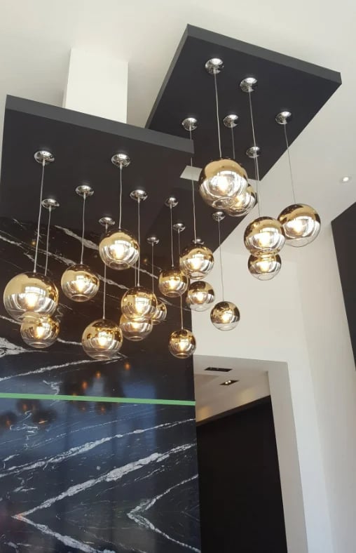 Modern pendant light fixture with multiple amber glass globes suspended from a dark ceiling above a black marble countertop