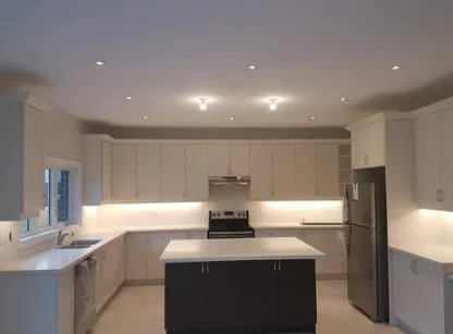 Modern kitchen with white cabinetry, black central island, stainless steel appliances, and recessed ceiling lights