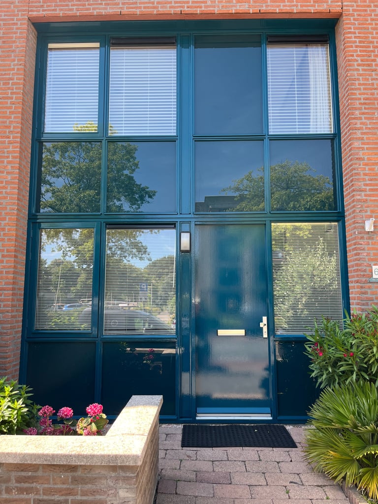 Donkerblauwe moderne glasdeur en kozijn in bakstenen pand met reflectie van bomen en lucht