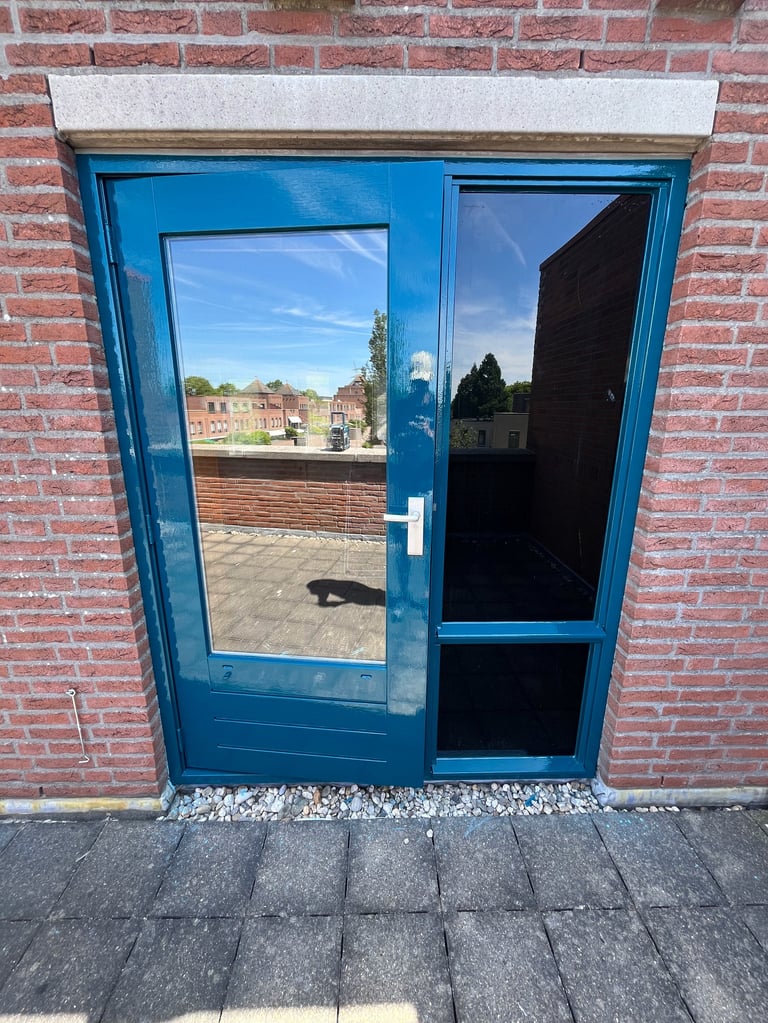 Blauwe dubbele deuren met glaspanelen in rode bakstenen muur met reflectie van binnenplaats en panden
