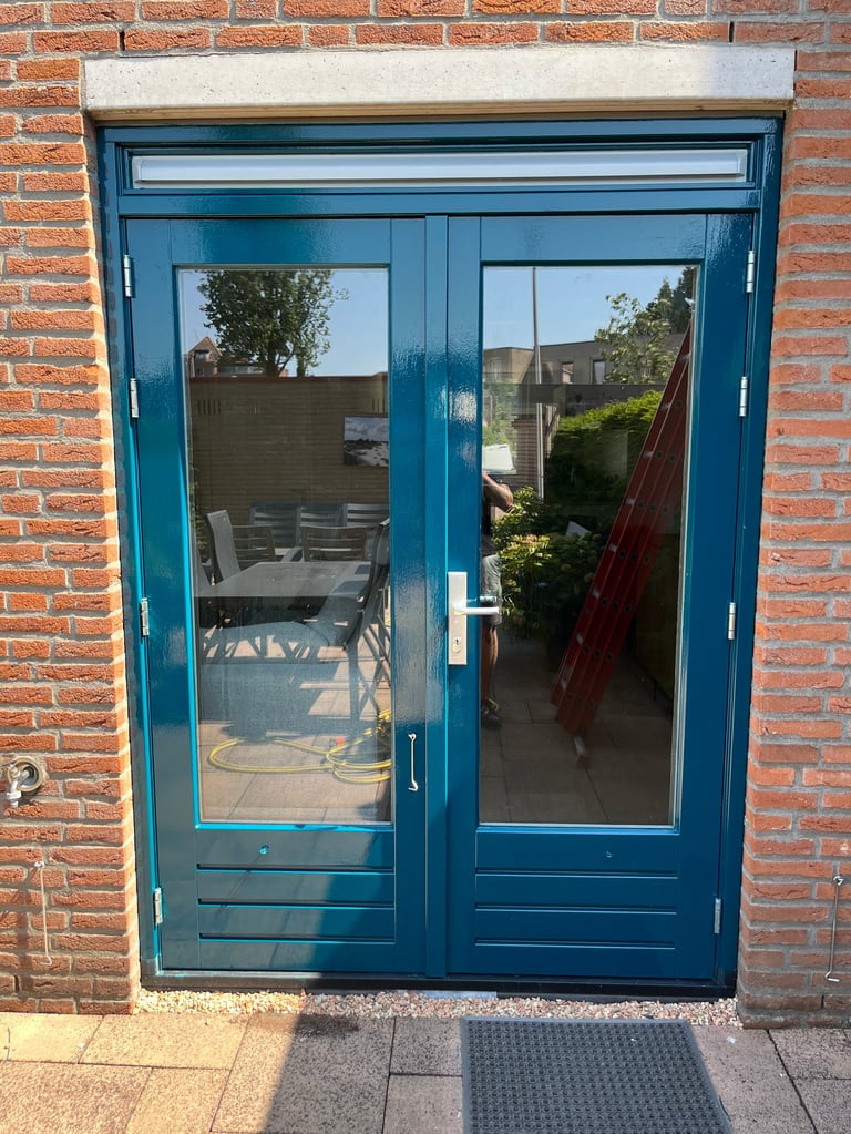 Blauwe dubbele glasdeuren in een rode bakstenen muur richting tuin