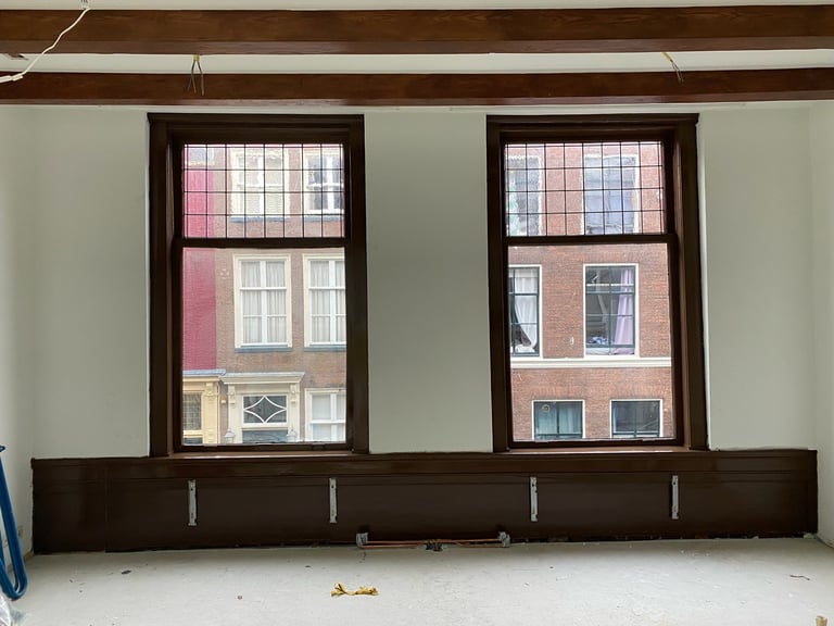 Interieur met twee grote donkere ramen, lichte muren en zichtbare houten balken
