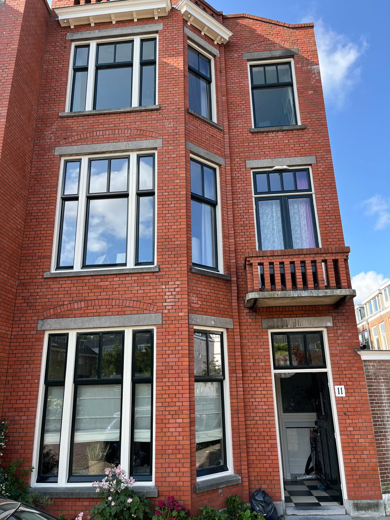 Drie verdiepingen tellend pand van rode baksteen met witte kozijnen en houten balkon