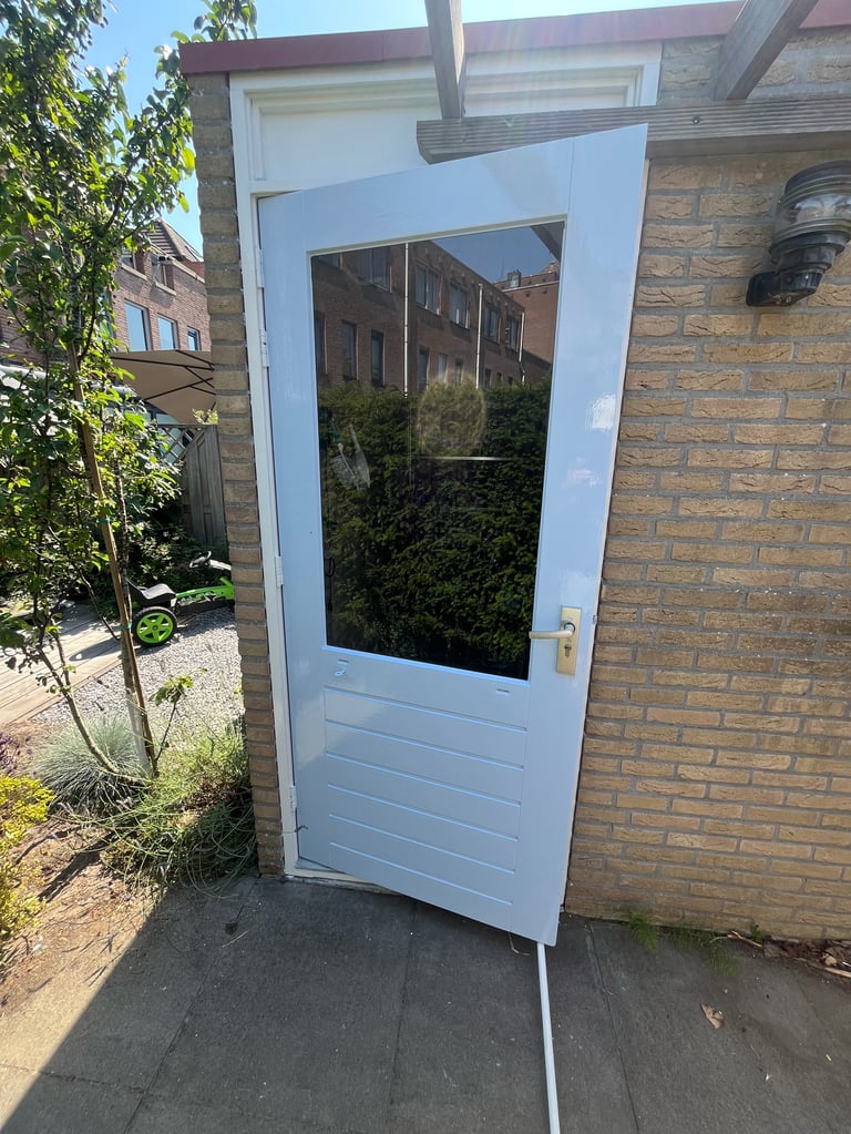 Lichtblauwe buitendeur met raam in bakstenen muur, weerspiegeling van bomen en panden