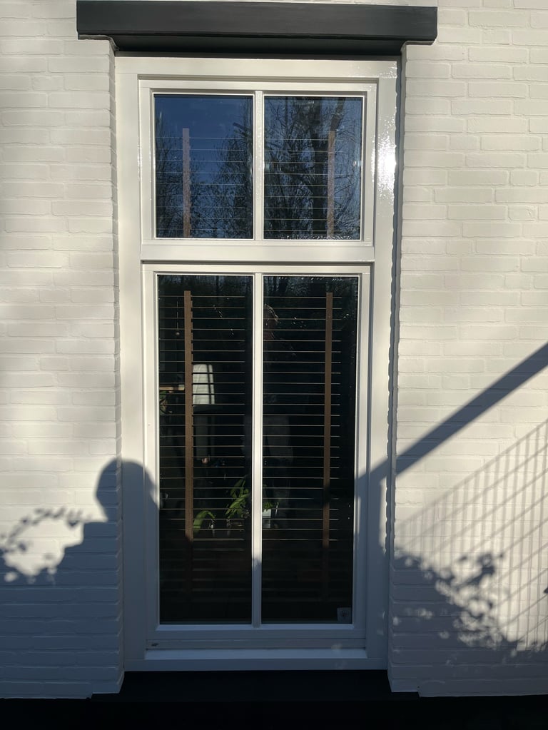 Witte glasdeur en kozijn op bakstenen muur met zwart afdakje en schaduwpartijen