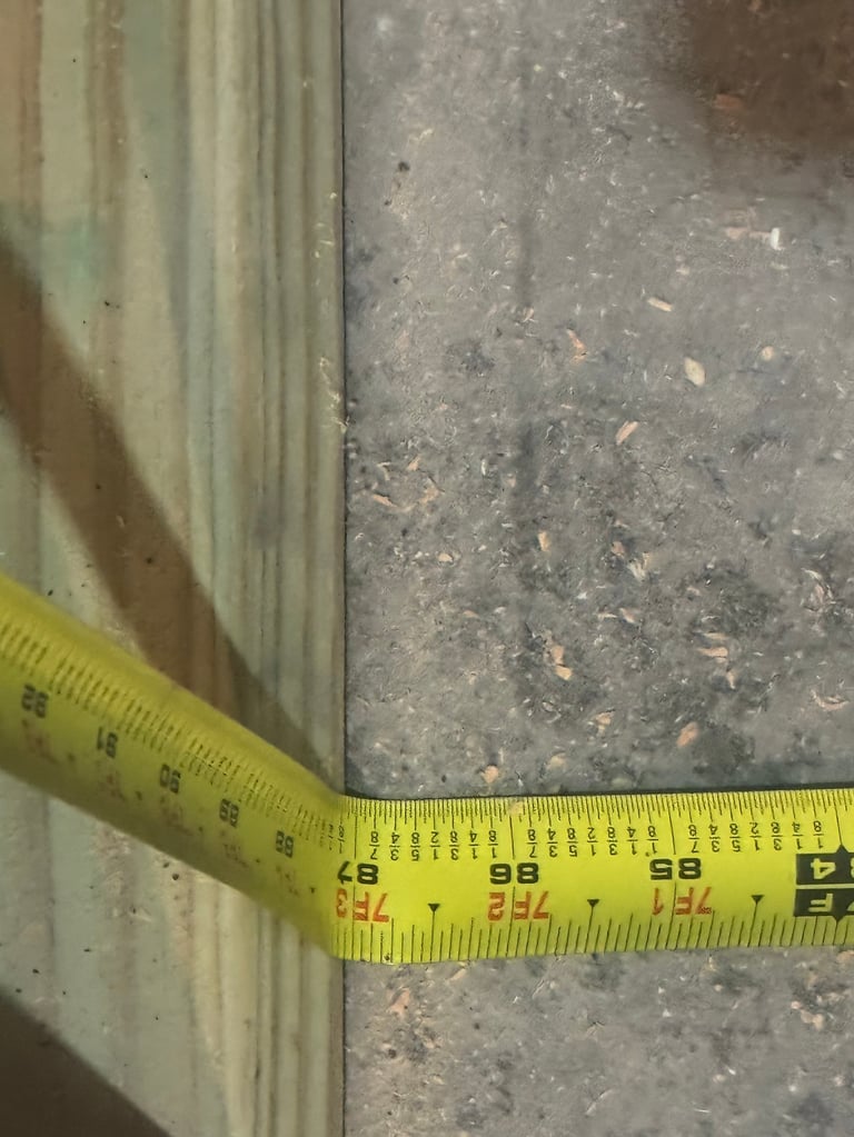 Yellow measuring tape laid across a gap between wooden and concrete surfaces