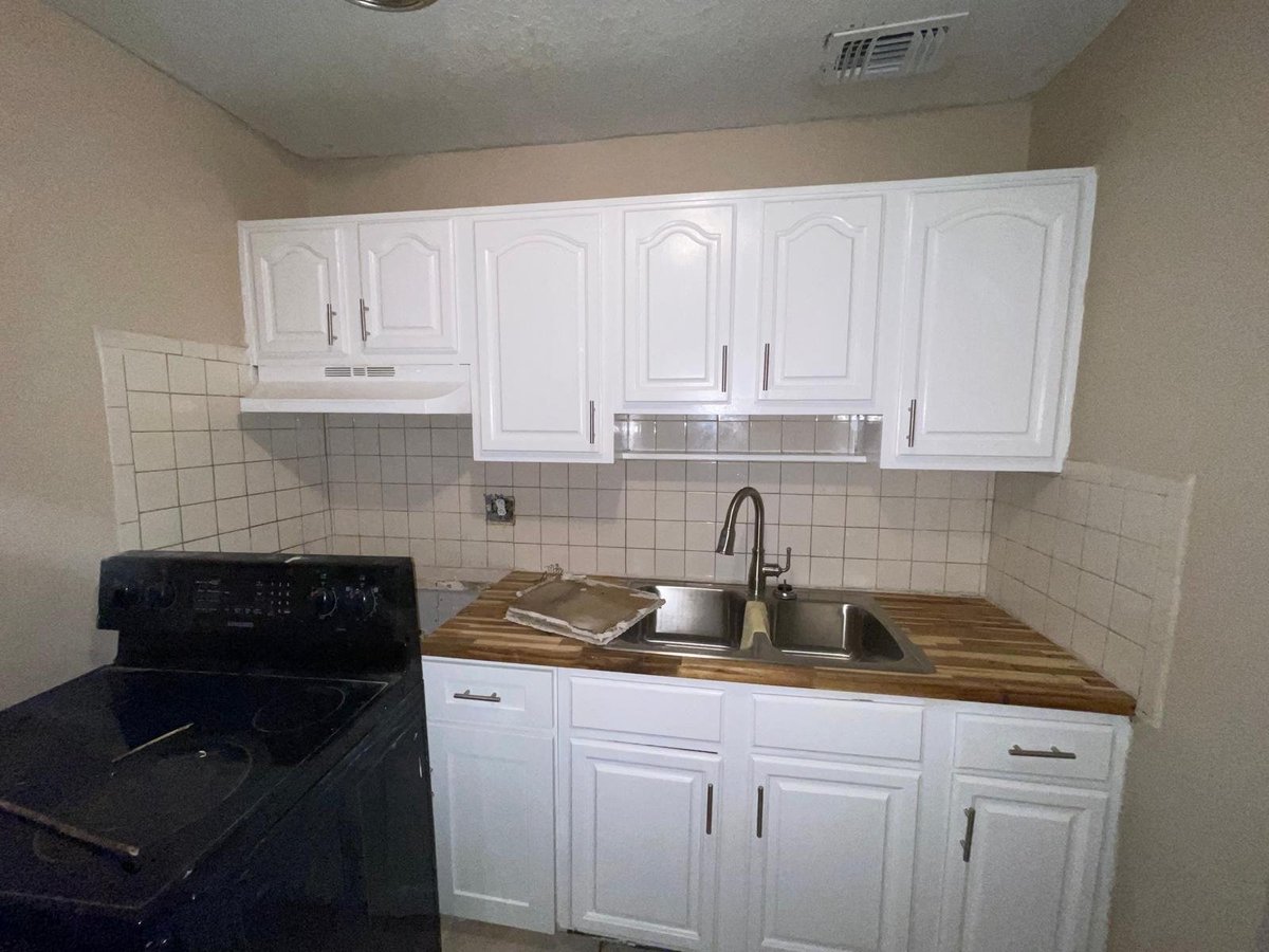 Small kitchen with white cabinets, black stove, sink with counter space, and white subway tile backsplash