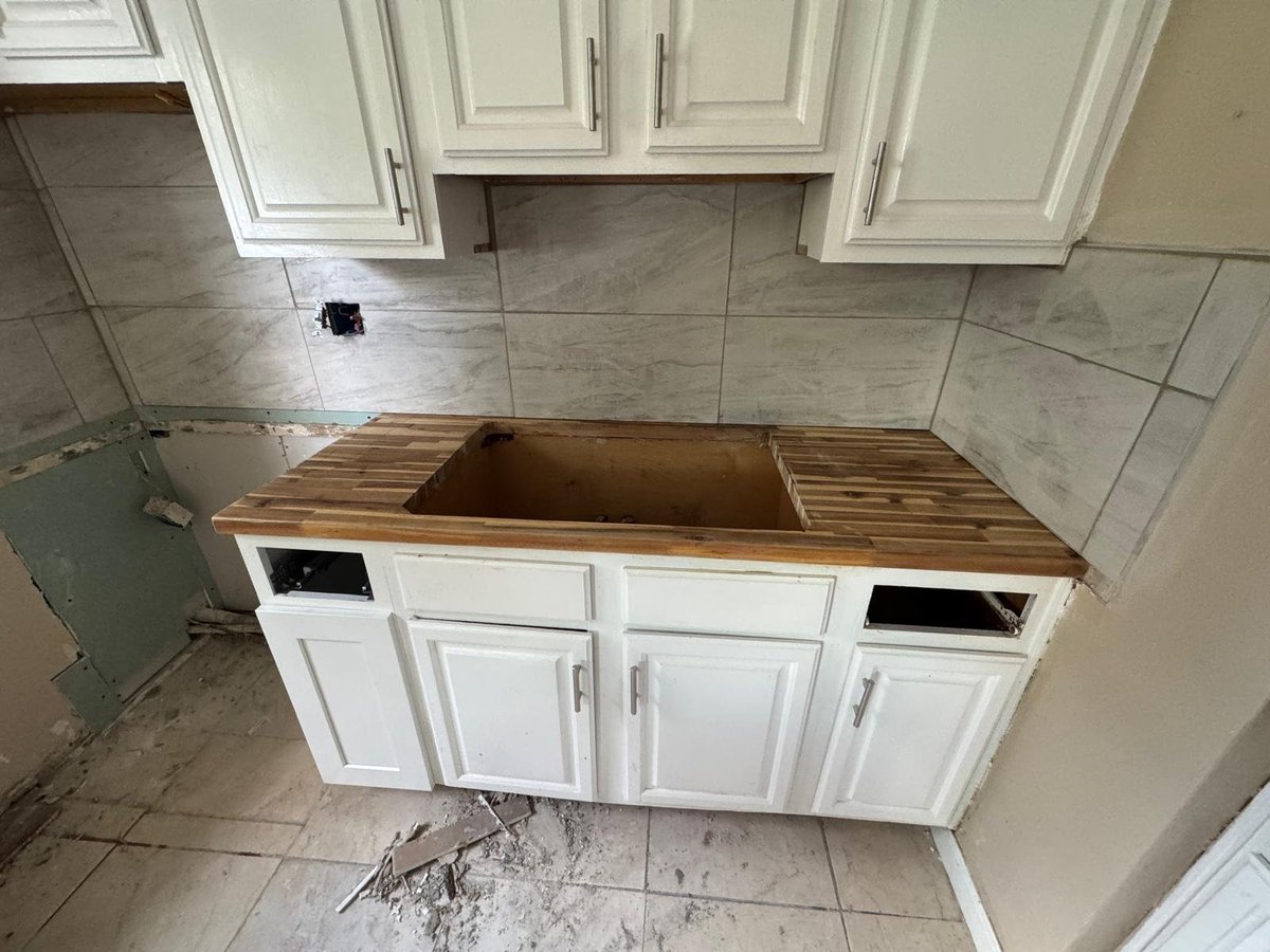 Kitchen sink basin under construction with white cabinetry and wooden countertop during renovation