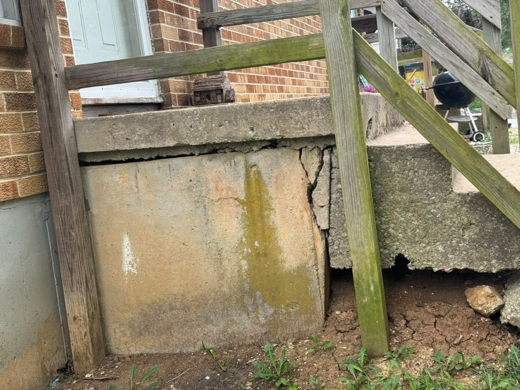 Weathered concrete water tank with moss and algae growth against brick wall with wooden fence frame