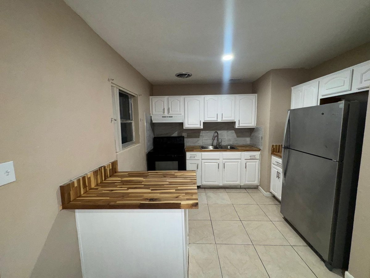 Modern kitchen interior with white cabinets, stainless steel appliances, wood countertop island, and beige tile flooring
