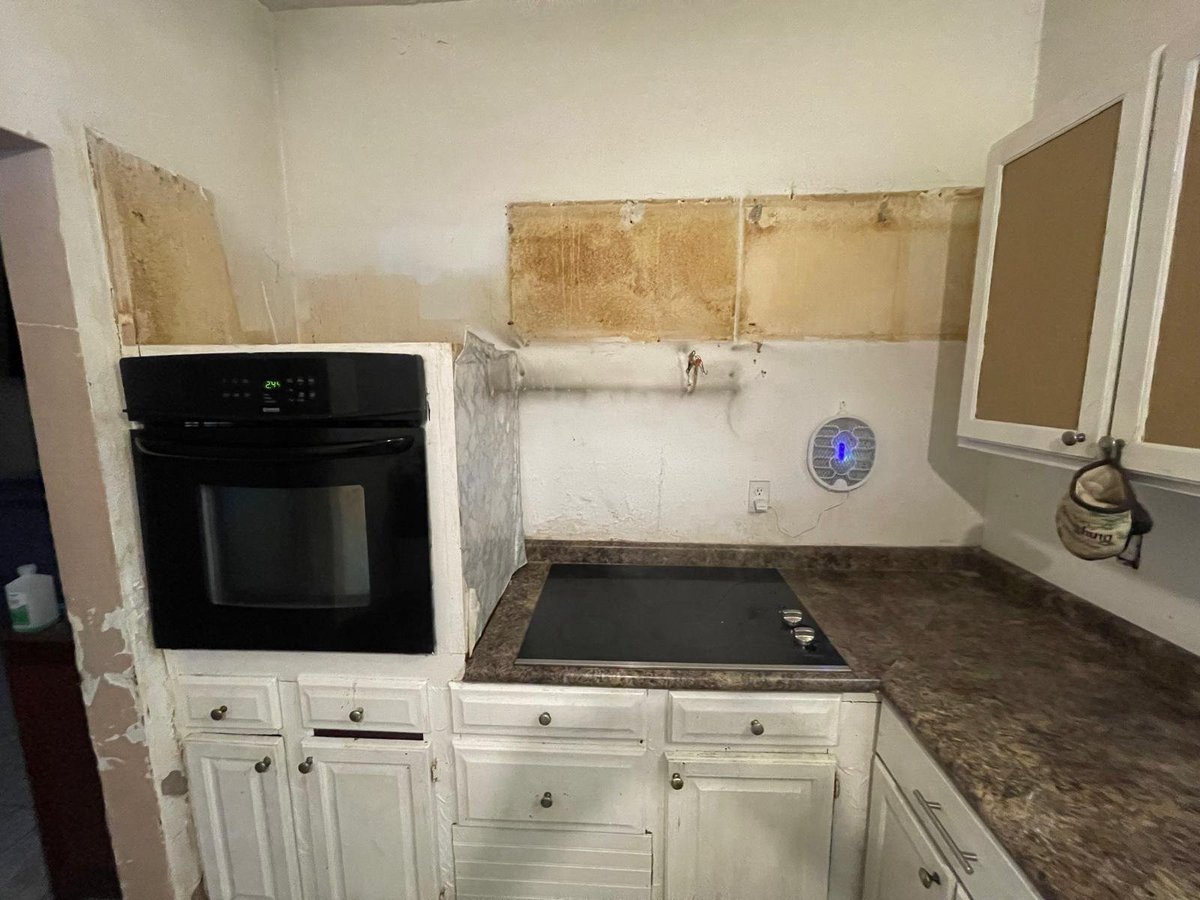A kitchen renovation in progress showing white cabinetry, a black oven, and walls with partial tile and drywall exposed during remodeling
