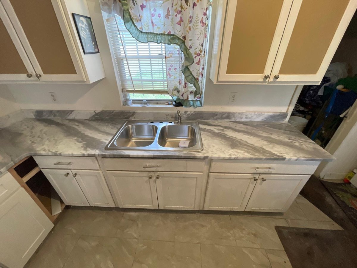 Kitchen sink with white cabinets and marble countertop under a window with floral valance