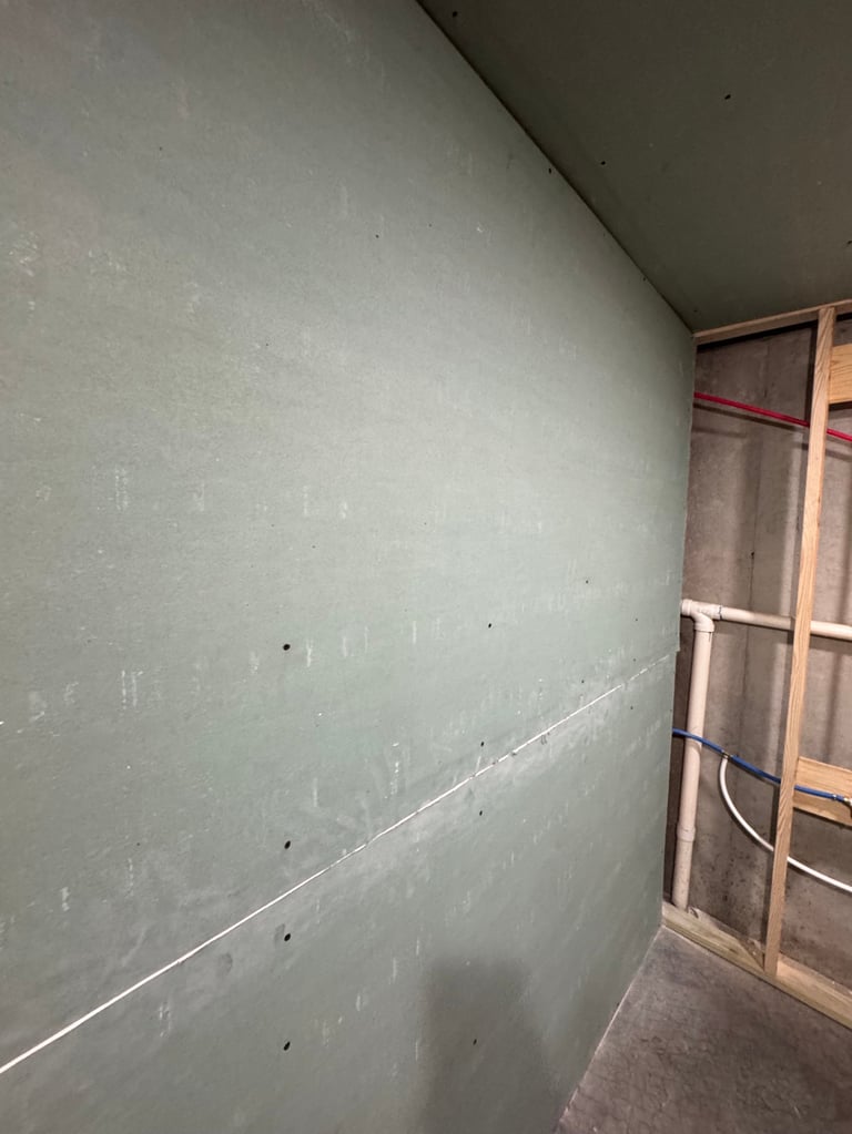 Interior construction showing drywall sheets on walls with joint tape and wooden framing visible in corner