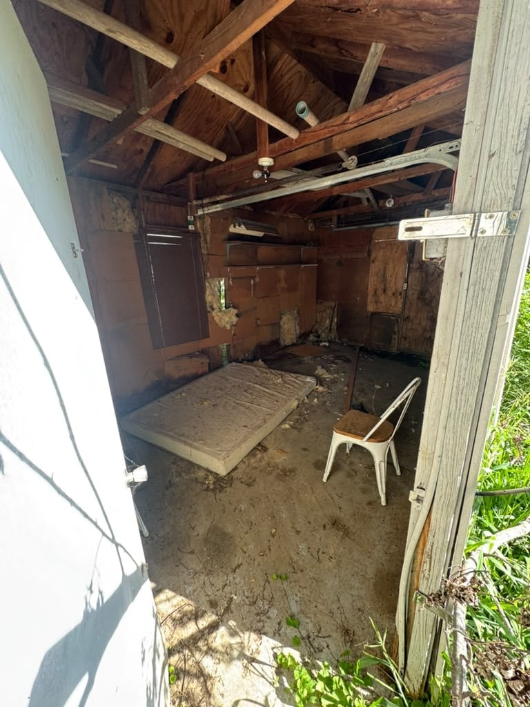 Interior of abandoned wooden shed with exposed beams, dirt floor, and weathered metal chair