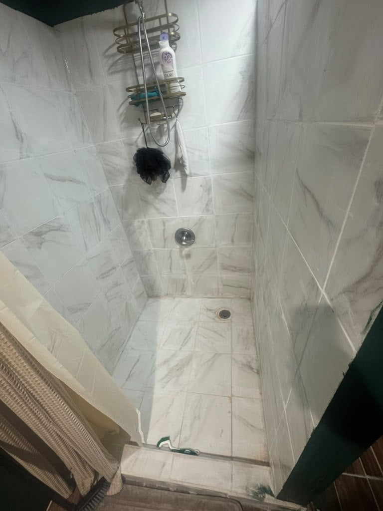 Narrow white marble tile shower stall with wall-mounted soap caddy and floor drain