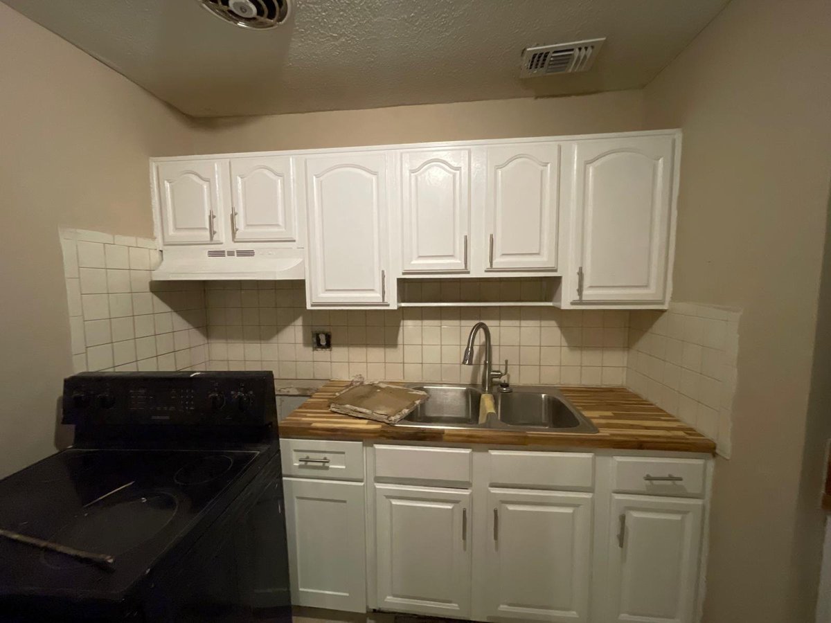 Small kitchen with white cabinets, black stove, wooden countertops, and stainless steel sink with faucet
