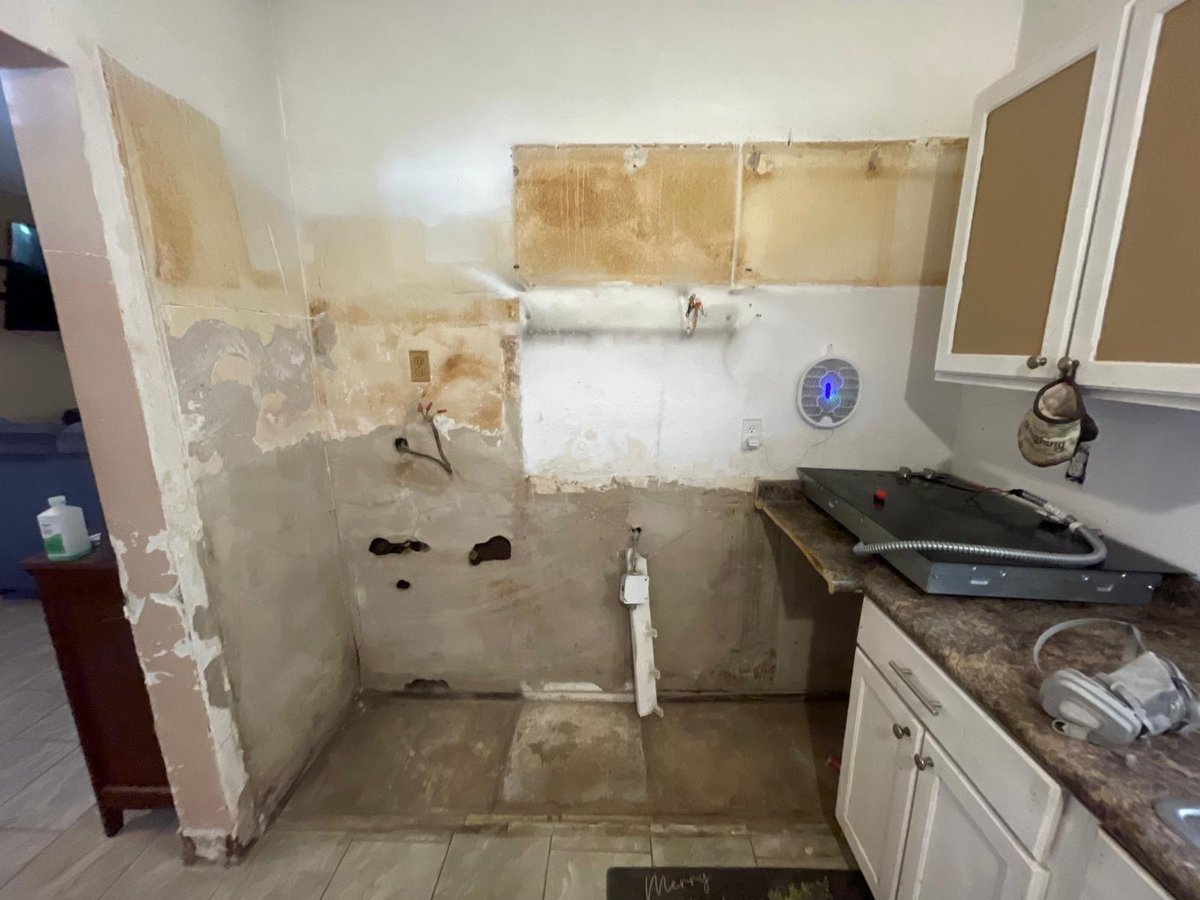 Bathroom under renovation with exposed walls, removed fixtures, and debris scattered on the floor
