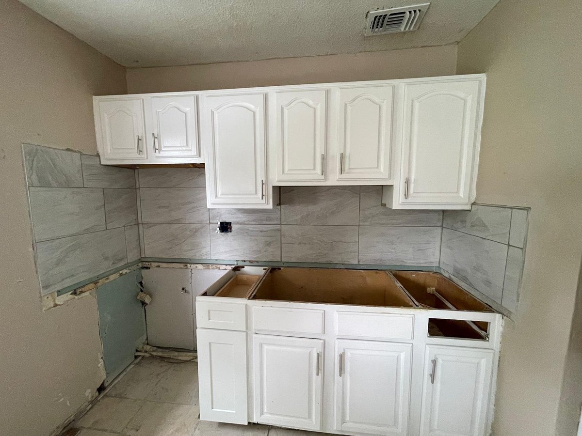 Unfinished kitchen renovation with white cabinetry, gray tile backsplash, and empty wooden counter space under construction