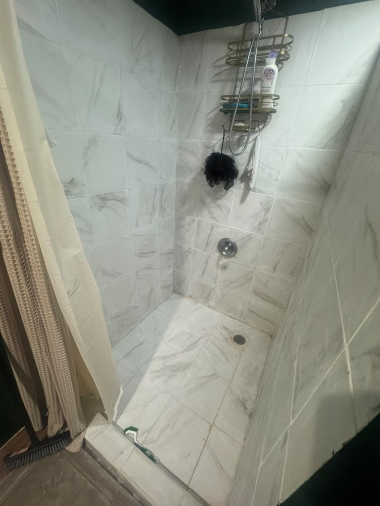 Modern shower enclosure with white marble-pattern tile walls, overhead rainfall showerhead, and multiple body sprays mounted on the wall