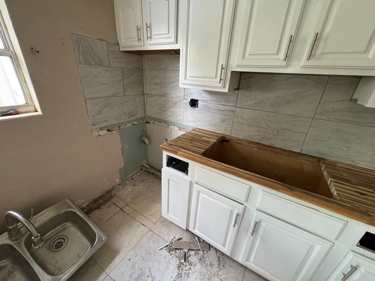 Kitchen under renovation with white cabinets, exposed countertop, tiled backsplash, and removal of appliances
