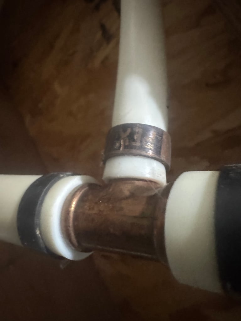 Close-up of copper pipe joint connecting white PVC pipes with metal bands