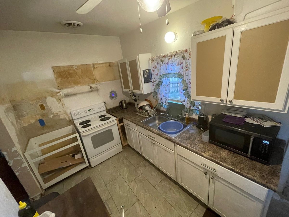 Kitchen undergoing renovation with exposed walls, white cabinets, granite countertop, and various appliances and construction materials visible