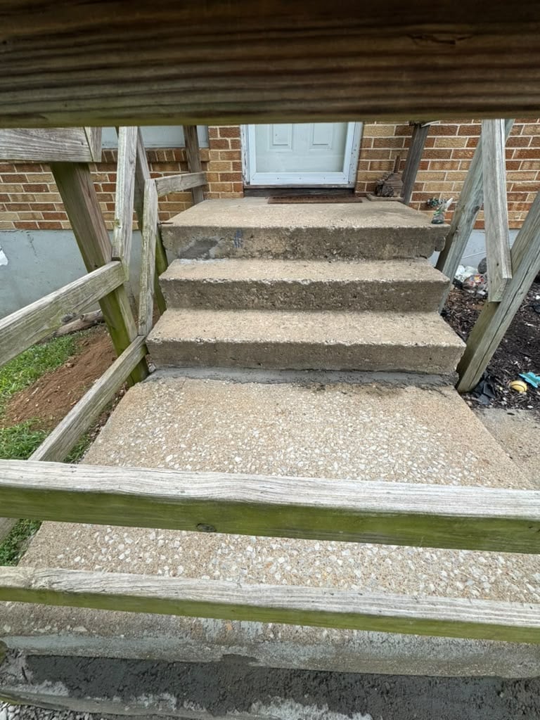 Concrete front porch steps with wooden railings leading to a brick house with white door