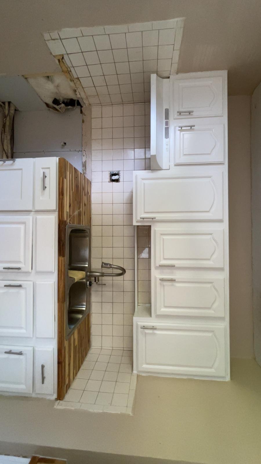 Overhead view of a galley kitchen with white cabinetry, wood-trimmed oven, and white subway tile backsplash