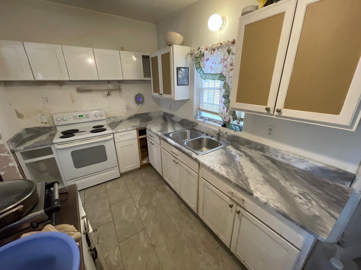 Small kitchen with white cabinets, electric stove, sink, and gray tile countertops and flooring