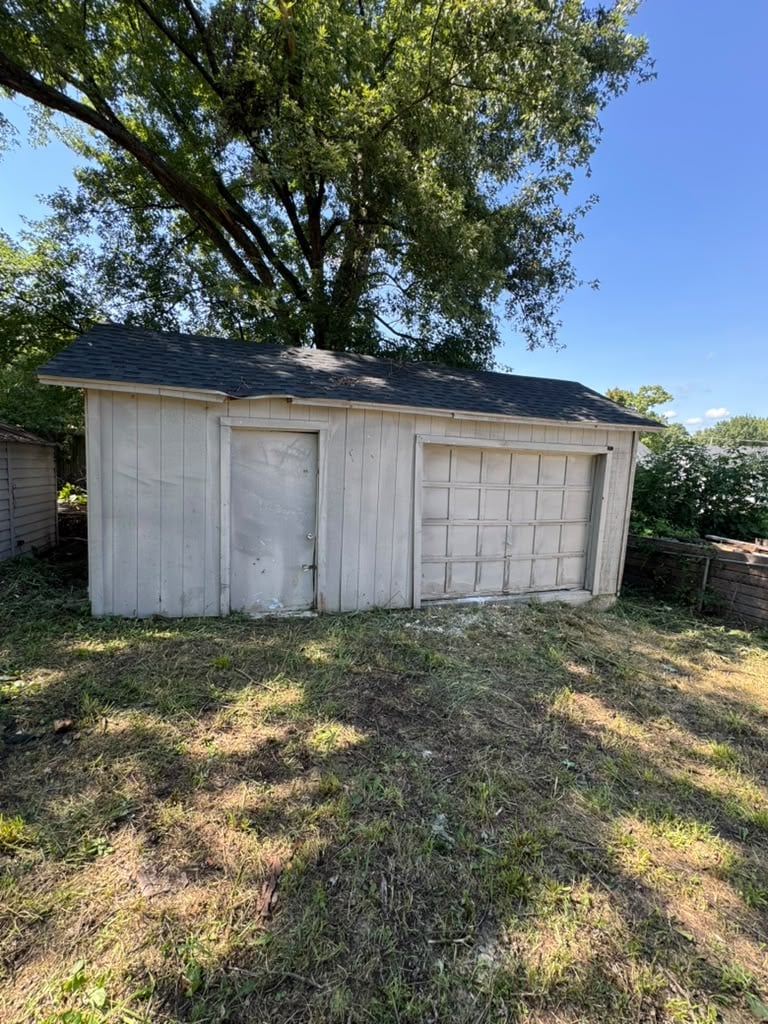 White wooden garage with two doors beneath a large tree and clear blue sky in a residential yard