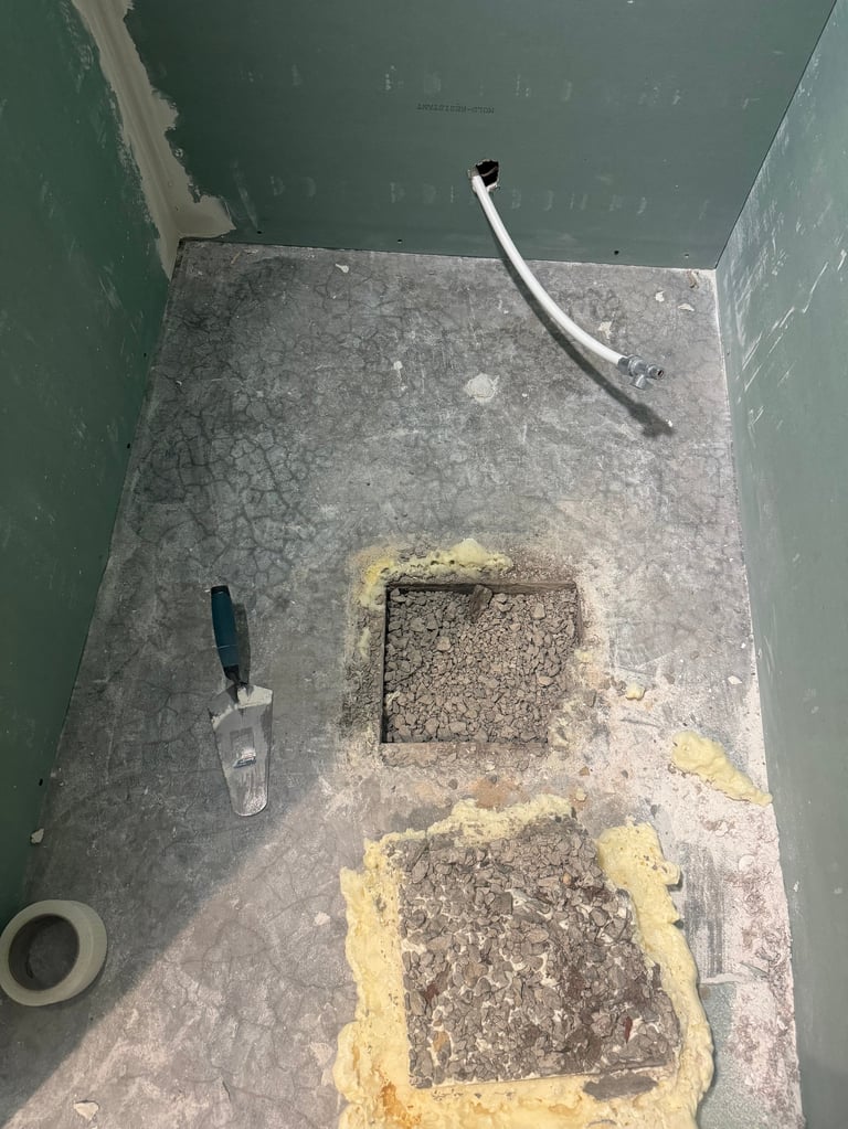 Overhead view of a bathroom corner with green walls gray tiled floor metal drainpipe and cleaning supplies