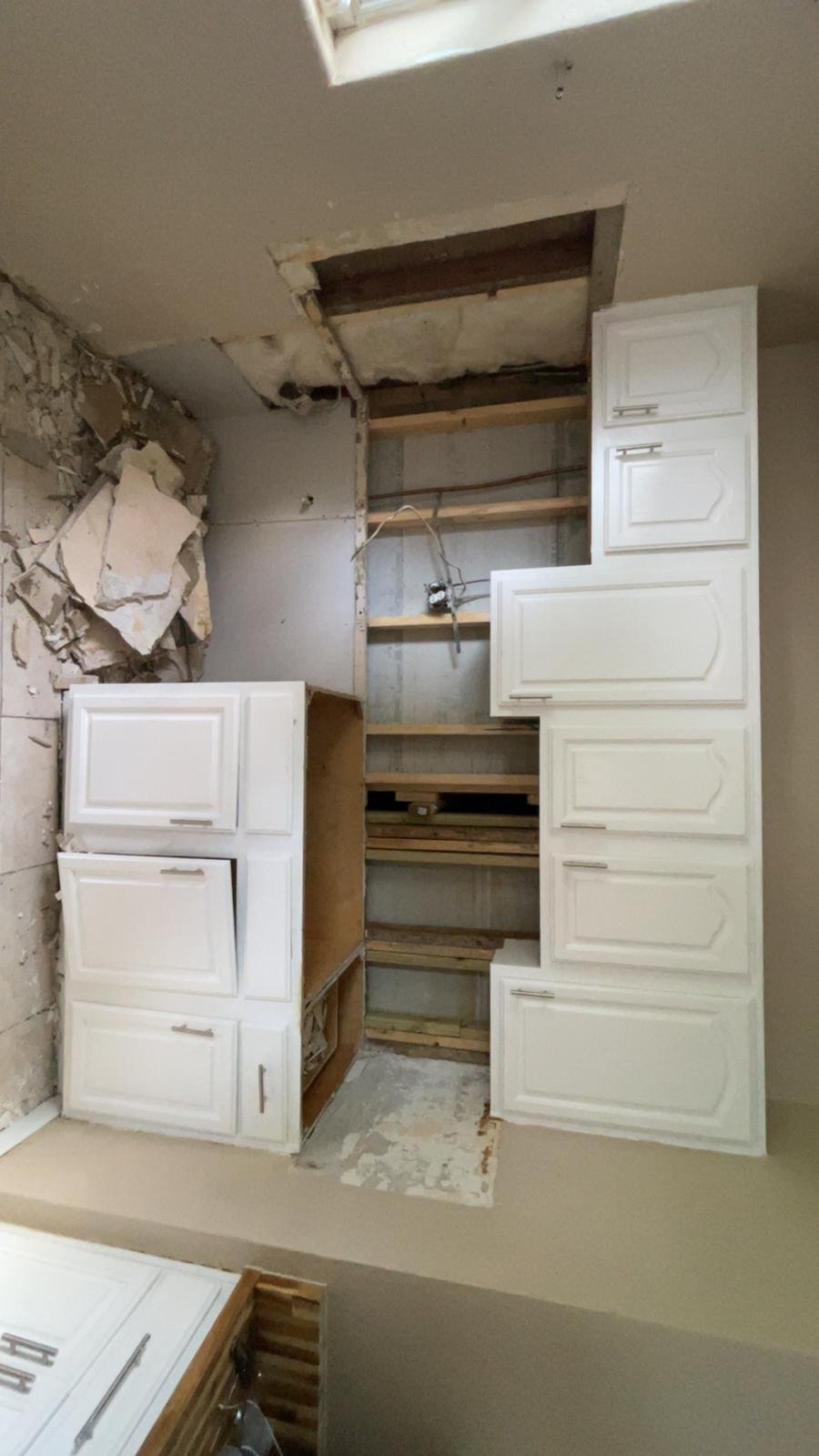 Kitchen cabinet installation in progress showing white cabinet doors and wooden frame structure against unfinished drywall