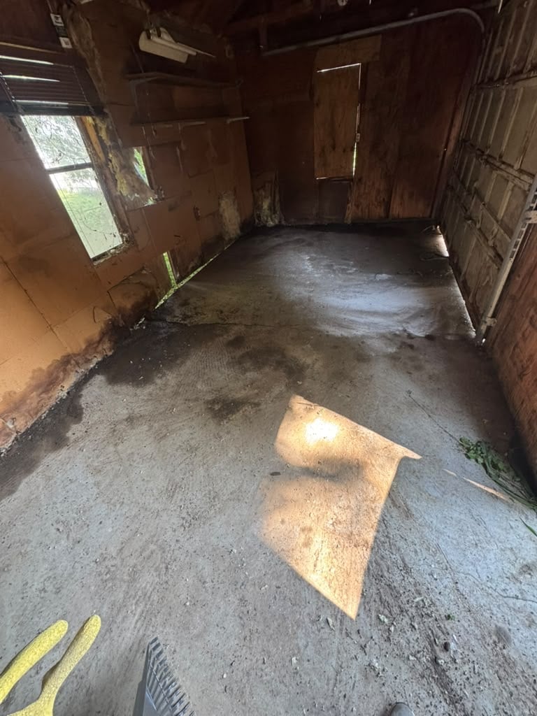 Empty interior of deteriorated metal shipping container or cargo trailer with concrete floor, rust stains, and sunlight streaming through side opening