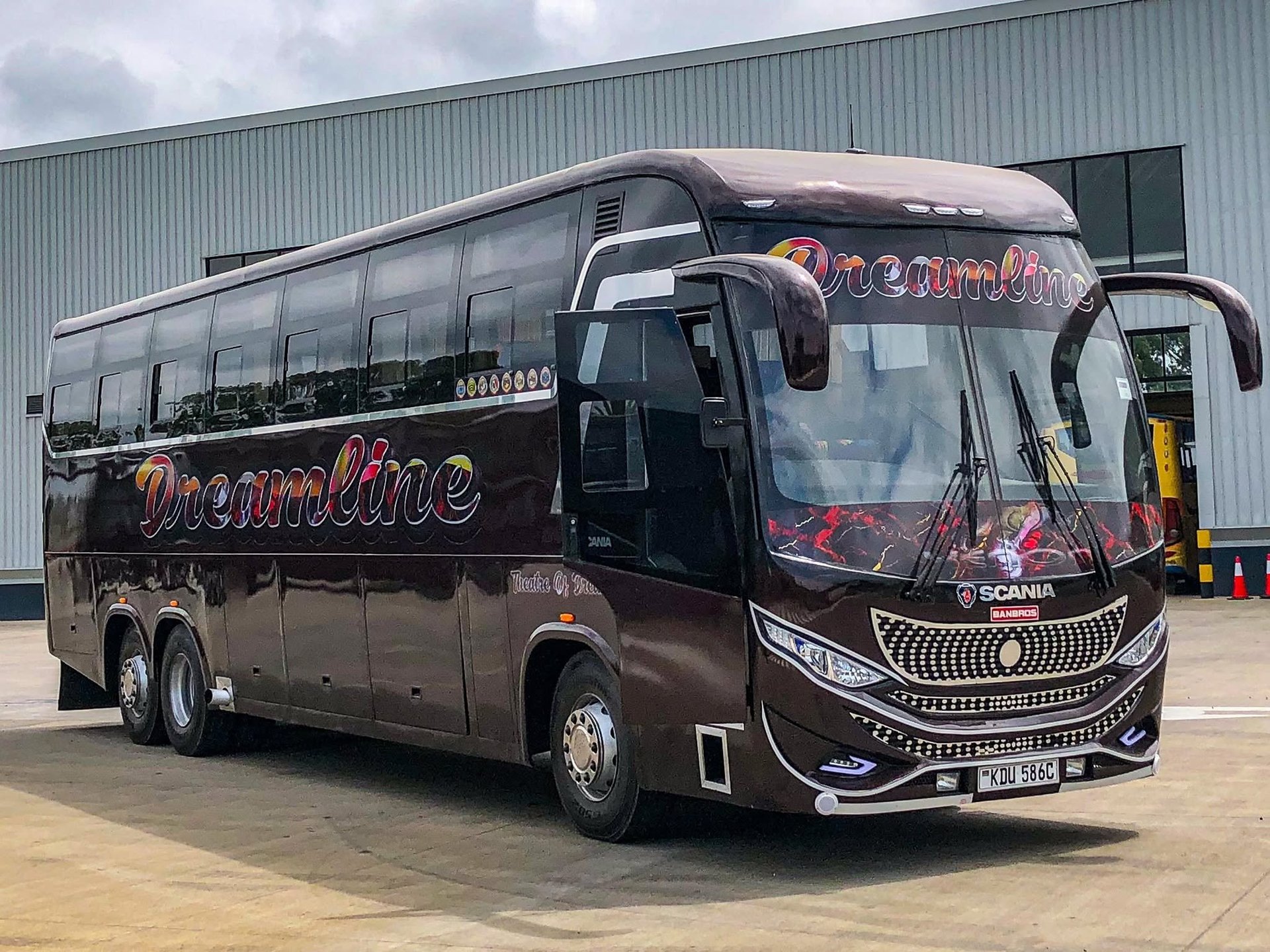 A large maroon and black luxury Dreamline coach bus parked in front of an industrial building