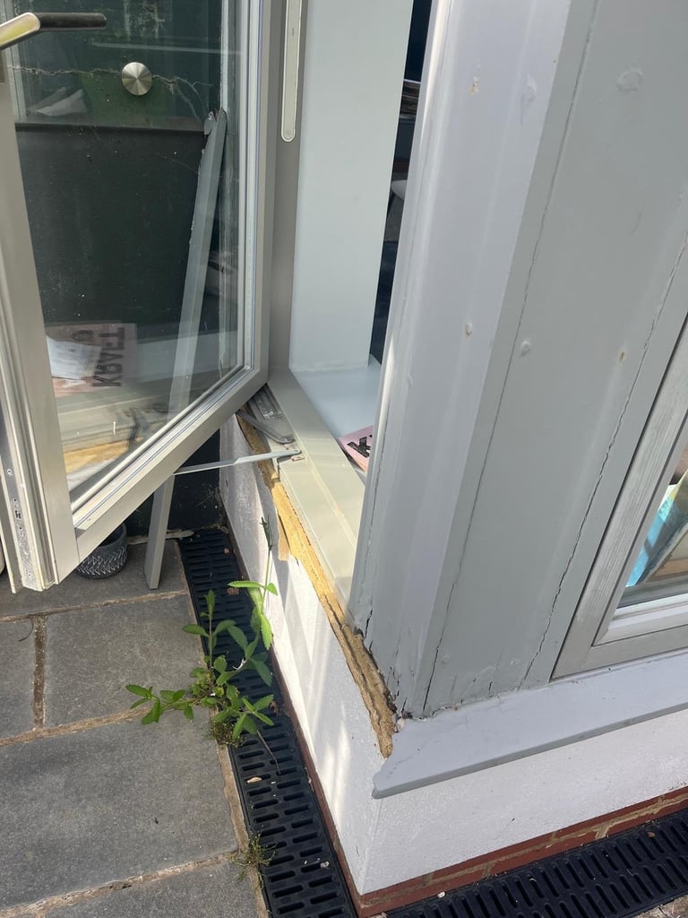 Open glass door with drainage grate and green plant shoots visible along the threshold