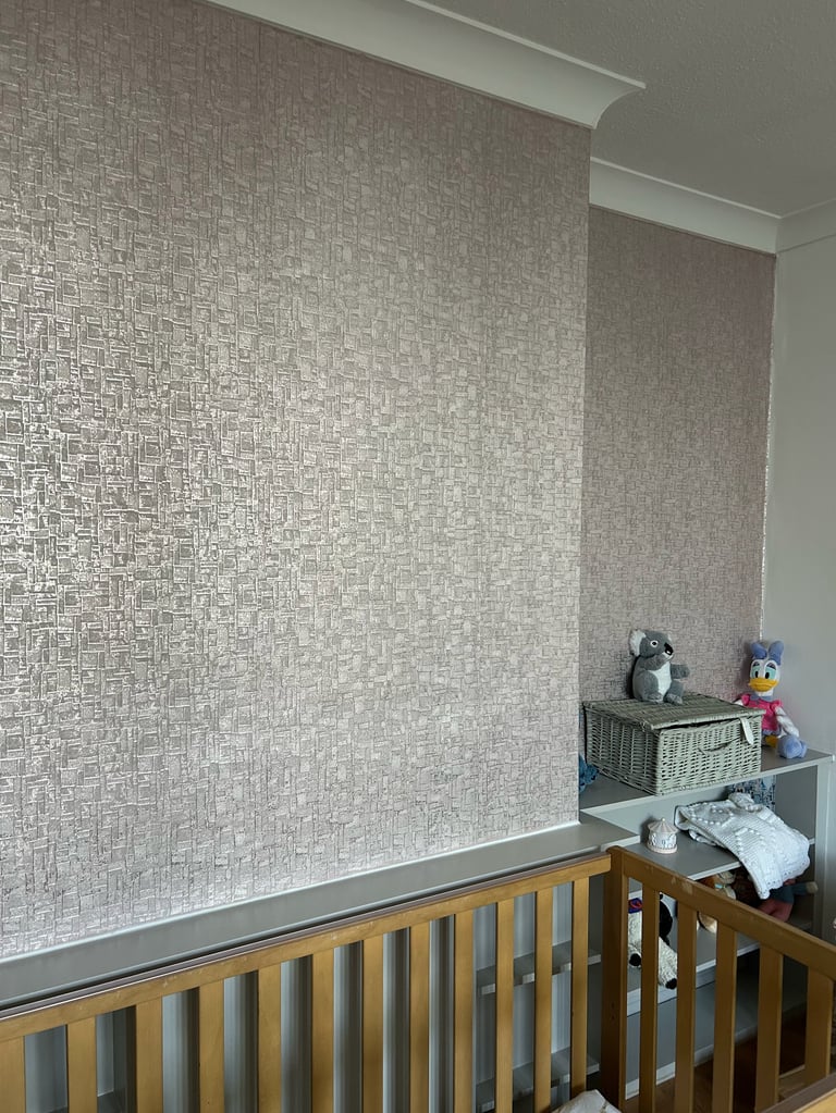Nursery room with wooden crib below textured gray wallpaper and wall shelves holding toys and supplies
