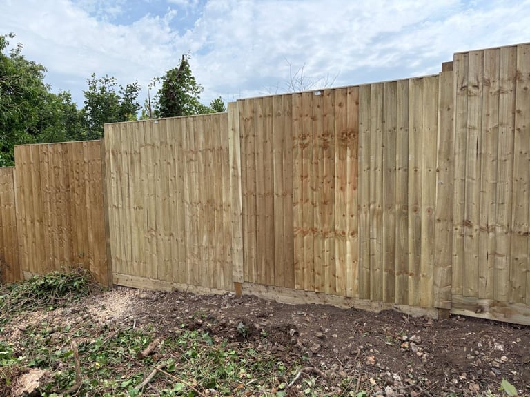 Newly installed wooden fence panels in a backyard with trees and clear sky in the background