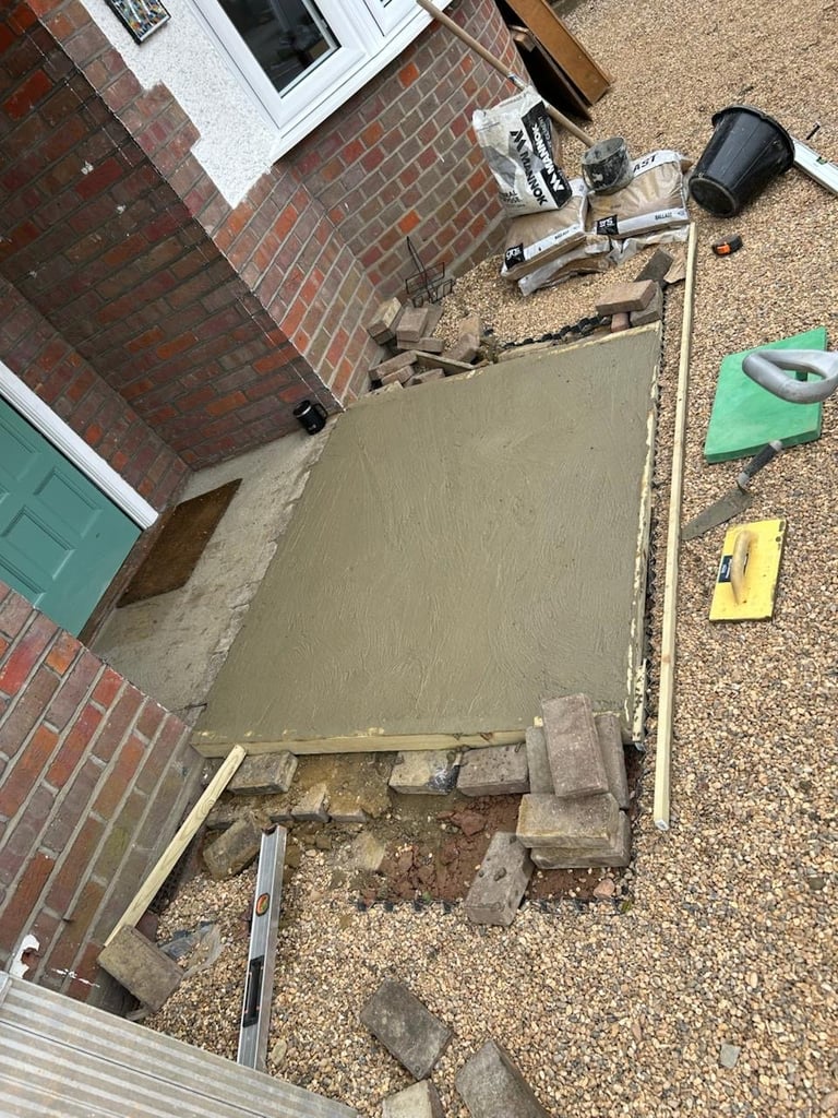 During — concrete patio being laid with wet cement, tools, and materials around the red brick building